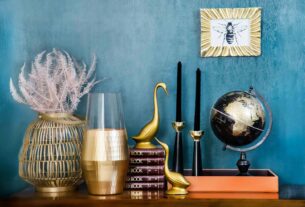 Stylish home decor arrangement including a globe, books, candles, and vases on a blue backdrop.