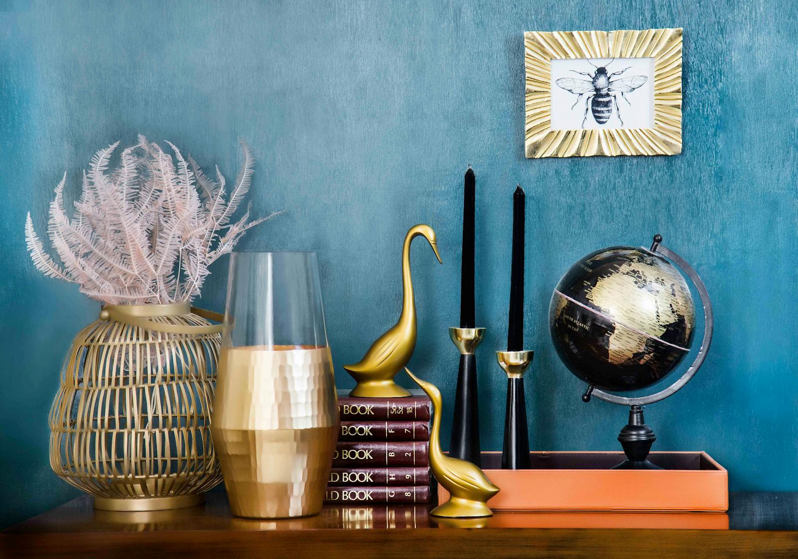 Stylish home decor arrangement including a globe, books, candles, and vases on a blue backdrop.